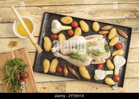 Gebratenes Huhn zum Braten mit frischem Knoblauch, Schalotten, Petersilie, Kirschtomaten, Kartoffeln und Olivenöl auf einem Blech Stockfoto