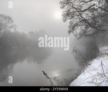 Sonne bricht durch den Nebel über dem Teviot River in Winterschnee in den Scottish Borders Stockfoto