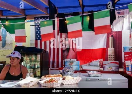 New York, New York, USA. September 2024. Das fest feiert das Leben des San Gennaro von Neapel, der Bischof von Benevento Italien war und 305 n. Chr. zum Märtyrer wurde. Das Little Italy Festival ist bekannt für italienische Gerichte wie Pizza, Würstchen, Cannolis, Zeppoles und vieles mehr. Alles Italienisch. Die berühmte Chefkochin Anne Burrell war der Grand Marshal. Eine Werbung guckt hinter einem Lebensmittelverkäuferstand heraus. (Kreditbild: © Milo Hess/ZUMA Press Wire) NUR REDAKTIONELLE VERWENDUNG! Nicht für kommerzielle ZWECKE! Stockfoto