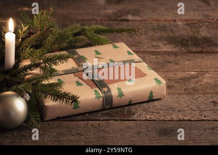 Weihnachtsdekoration mit Geschenkbox in klassischem braunem Papier, grünen Tannenzweigen, Weihnachtskugel und beleuchteter Kerze auf einem Vintage-Holztisch Stockfoto