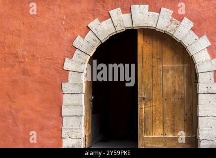 Antike gewölbte Eingang mit doppelten Holztüren, linke Seite geöffnet, und der Orange-rosa Wand Stockfoto