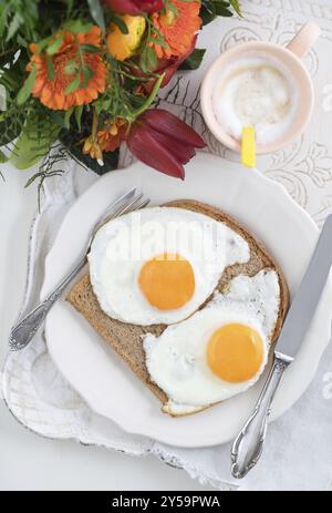 Frühstück mit Spiegeleiern, Cappuccino und einen Blumenstrauß auf einem Tablett Stockfoto