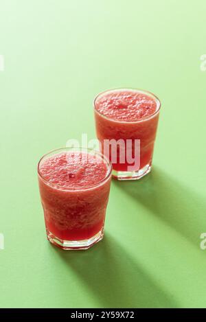 Süßer Wassermelonenschlamm auf grünem Hintergrund bei rauem Licht. Zwei Gläser Wassermelonen Eisgetränk. Sommermocktail. Erfrischendes Getränk Stockfoto