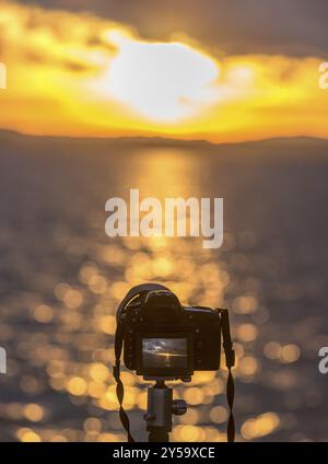 Bild mit einer modernen DSLR-Kamera zugeschnitten, auf einem Stativ stehend und im Live View-Modus mit Sonnenuntergang über dem Wasser fotografiert Stockfoto