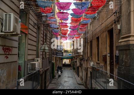 Catania, Italien - 20. Mai 2024: Kunst über der Straße: Eine dekorierte Gasse mit leuchtenden Sonnenschirmen, die den kreativen Geist von Catania einfangen. Stockfoto