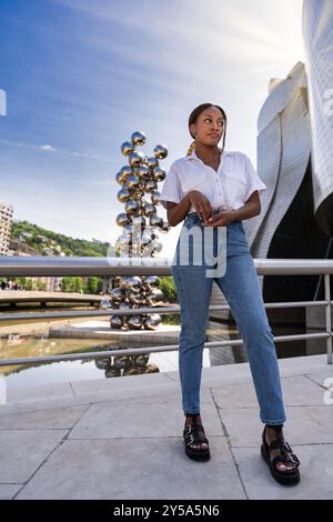 Junge Frau posiert an einem Geländer mit dem guggenheim Museum bilbao und einer Welpenskulptur von jeff koons im Hintergrund Stockfoto