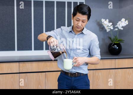 Kaffee aus der französischen Presse in den Becher gießen, asiatischer Mann in Geschäftskleidung in der Büroküche Stockfoto