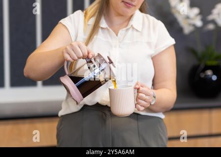 Kaffee aus der französischen Presse in den Becher gießen, Frau, die im Büro ein Getränk zubereitete Stockfoto