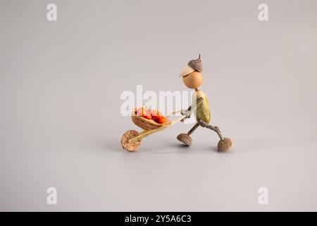 Handgefertigte herbstliche Figur aus Eicheln, Schubkarre mit Beerenfüllung, DIY-Konzeptkunst, Aktivitäten für Kinder, Natur inspirierte Dekoration, Herbst cr Stockfoto