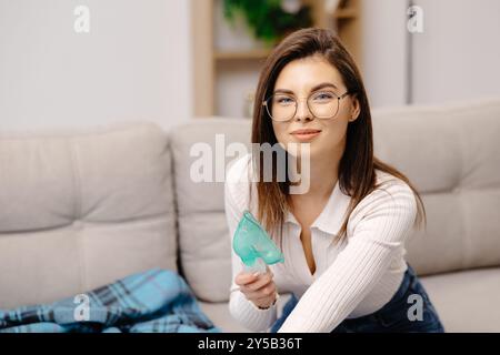 Eine junge Frau, die einen Maskenvernebler hält, der Dämpfe in die Lunge einatmet. Kaukasische kranke Dame, die zu Hause durch Inhalationsmaske einatmet. Selbstbehandlung o Stockfoto