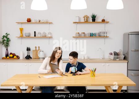 Eine junge Frau hilft einem Jungen beim Unterricht mit einem Tablet und einem Globus. Ein Schüler macht seine Hausaufgaben mit Hilfe eines Tutors. Stockfoto