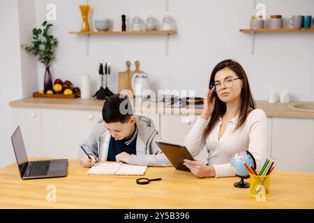 Eine junge Frau hilft einem Jungen beim Unterricht mit einem Tablet und einem Globus. Ein Schüler macht seine Hausaufgaben mit Hilfe eines Tutors. Stockfoto