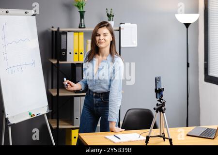Junge Frau Mentorin nimmt Präsentationen auf, Webinar über Smartphone auf Stativ stehend, Lehrer Coach erklärt, hält Online-Unterricht, mit Telefon-Webc Stockfoto