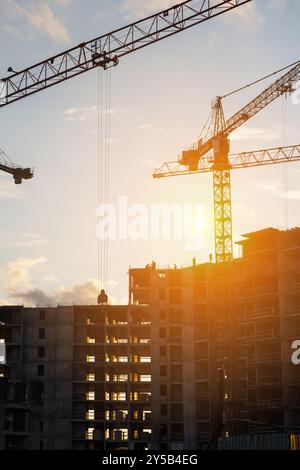 Bei Sonnenuntergang arbeiten Krane auf einer Baustelle, während die Arbeiter aktiv am Bau des Bauwerks beteiligt sind Stockfoto