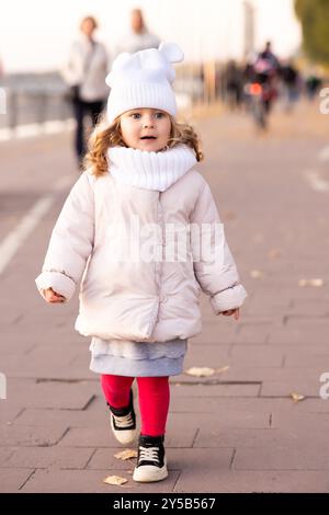 Das kleine lustige Mädchen rennt und lächelt auf gelben Bäumen im Herbstpark. Vorschulmädchen läuft und lacht auf der Parkallee. Stockfoto