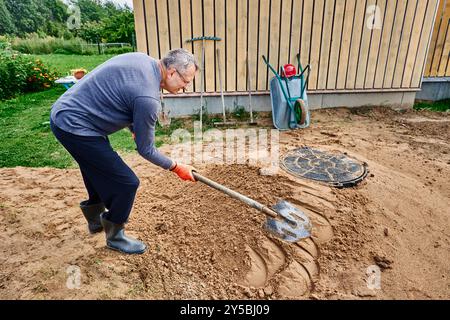 Bauarbeiter schlägt Schaufel auf Sandhaufen um den Rand des Klärgrubenkanals, um es zu verdichten. Stockfoto