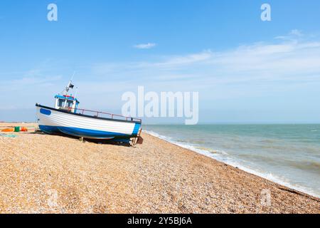 Ein kleines Fischerboot an einem Kiesstrand mit Meer im Hintergrund an einem klaren, sonnigen Tag in Dungeness Kent UK Stockfoto