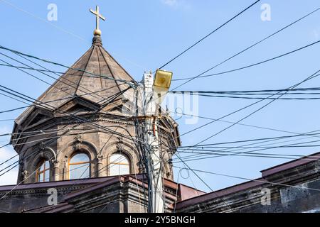 Straßenlaterne Pfosten mit vielen verwickelten elektrischen Kabeln und Drähten und Kuppel der Kathedrale der Heiligen Mutter Gottes im Hintergrund in Gyumri Stadt, Armenien Stockfoto