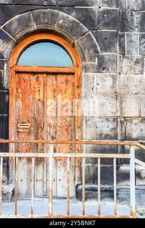 Schäbige orange lackierte Holztür des Wohnhauses aus schwarzem Tuff in der Abovyan Straße in der Altstadt von Gyumri Stadt, Armenien in der Sommerdämmerung Stockfoto