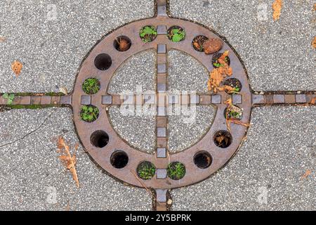 Kreisförmiger rostiger Mannlochdeckel mit Pflanzen, Betonfußsteig, Herbstlaub, städtisches Detail-Konzept Stockfoto