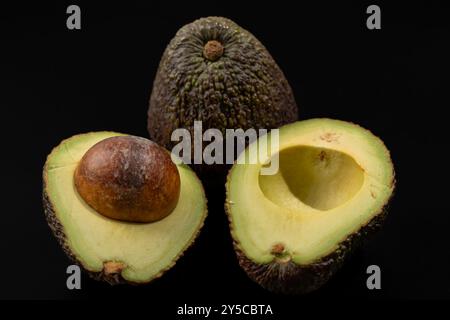 Abgebildet sind zwei Avocados, von denen einer in zwei Hälften geschnitten ist. Das Konzept der Fülle und Frische als Avocado ist eine gesunde und beliebte Frucht. Stockfoto
