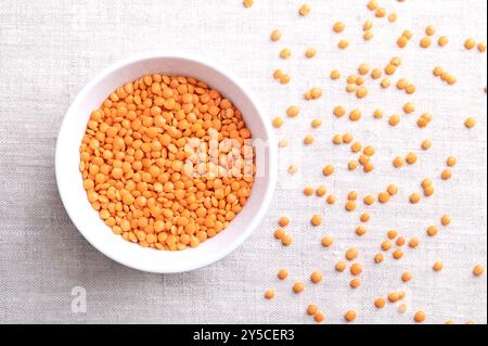 Rote Linsen in einer weißen Schüssel auf Leinen. Linsensorte mit entfernter Schale für eine kürzere Garzeit und um Einweichen zu vermeiden. Getrocknete Früchte von Lens culinaris Stockfoto