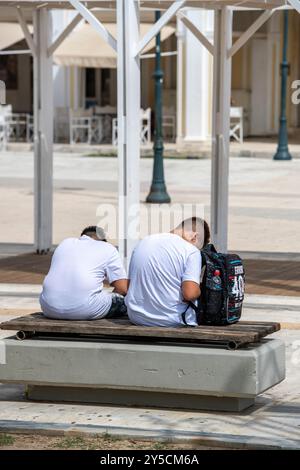 Zwei junge Jungs sitzen an einer Wand in Zakynthos, Griechenland, die beide Handys benutzen und sich völlig in das einfühlen, was sie tun Stockfoto