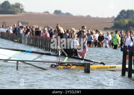 Mersea Island, Großbritannien. September 2024. Das jährliche Rennen um die Insel fand heute um Mersea Island in Essex statt. Segelschiffe aller Art nehmen an der Veranstaltung Teil. Die Besatzungen müssen ihre Boote über den Strood transportieren, der einzigen Straße auf und vor der Insel, die bei außergewöhnlich hohen Fluten überschwemmt wird. Credit:Eastern Views/Alamy Live News Stockfoto