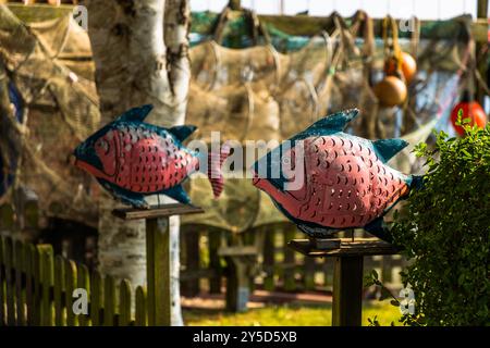 Bunter Metall-Dekofisch steht neben Fischfallen an einem Steg in Arnis, Deutschlands kleinster Stadt. Die Dekoration erinnert an die maritime Tradition der Stadt an der Schlei. Lange Straße, Schleswig-Holstein, Deutschland. Stockfoto
