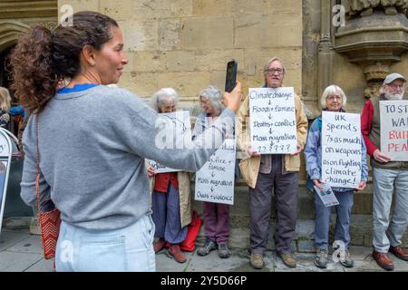 Bath, UK. September 2024. Ein Tourist wird fotografiert, der vor einem protestmarsch durch das Zentrum von Bath Demonstranten fotografiert. Der Protest "Kampf gegen den Klimawandel - Krieg nicht anheizen" wurde von der Extinction Rebellion Bath und der Bath-Gruppe "Stop war" organisiert und fand statt, um die Tatsache zu unterstreichen, dass Großbritannien sieben Mal so viel für Waffen ausgibt wie für den Klimawandel. Quelle: Lynchpics/Alamy Live News Stockfoto