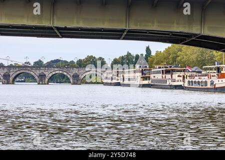 Touristenboote liegen am Dammkai entlang der Maas, Sint Servaasbrug Brücke im Hintergrund, ruhiges Wasser, bewölkter Tag in der Stadt Maastricht in Sout Stockfoto