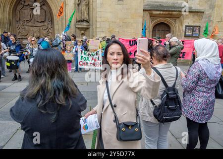 Bath, UK. September 2024. Ein Tourist macht ein Selfie vor Demonstranten vor der Bath Abbey vor einem protestmarsch durch das Zentrum von Bath. Der Protest "Kampf gegen den Klimawandel - Krieg nicht anheizen" wurde von der Extinction Rebellion Bath und der Bath-Gruppe "Stop war" organisiert und fand statt, um die Tatsache zu unterstreichen, dass Großbritannien sieben Mal so viel für Waffen ausgibt wie für den Klimawandel. Quelle: Lynchpics/Alamy Live News Stockfoto