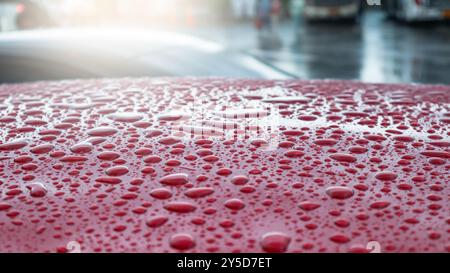 Während der Regenzeit liegen die Regentropfen sanft auf der Oberfläche eines roten Autodachs, reflektieren das sanfte Licht und schaffen eine ruhige, frische Atmosphäre Stockfoto