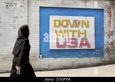 Schwarzer Schleier mit muslimischer Frau, die an antiamerikanischen Wandgemälden vor der alten amerikanischen Botschaft in teheran, iran, vorbeiläuft Stockfoto