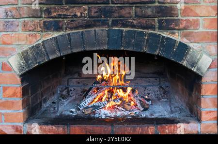 Traditioneller Backofen zum Kochen und Backen von Speisen. Brennholz brennt im Ofen. Holzofen. Bild eines Backsteinpizzaofens mit Feuer. Flammen und Stockfoto