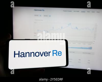 In dieser Fotoabbildung hält eine Person ein Mobiltelefon mit dem Logo der deutschen Rückversicherungsgesellschaft Hannover Rück SE vor der Business-Website. Stockfoto