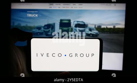 In dieser Abbildung hält eine Person ein Mobiltelefon mit dem Logo des italienischen Nutzfahrzeugunternehmens Iveco Group N.V. vor der Webseite. Stockfoto