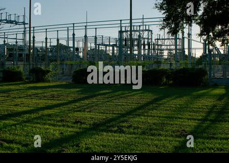 Elektrische Umspannstation, umrahmt von Baumschenkeln, niedriger, breiter Blick über hellgrünes Gras und Bäume am späten Nachmittag Sonne mit langem Schatten. Nahe Sonnenuntergang grün Stockfoto