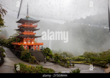 Die 3-stöckige Pagode des Nachisan Seiganto-JI-Tempels mit Nachi Falls im Regen unter einem Regenschirm, April, Japan Stockfoto