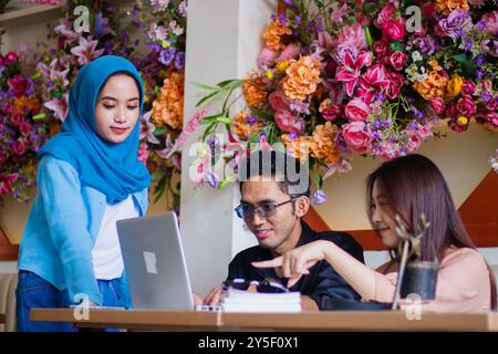 Eine Gruppe lächelnder indonesischer Freelancer konzentriert sich auf Brainstorming und Chats, während sie in einem Café an einem Unternehmensauftrag arbeiten. Für gr Stockfoto