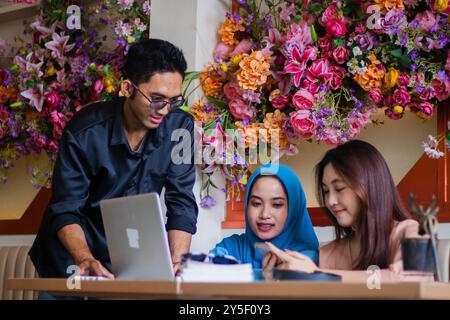 Eine Gruppe asiatischer Studenten hört auf einem Handy vor einem Laptop eine Präsentation von einem Dozenten in einem Café. Für Gruppenkonzept COMPA Stockfoto