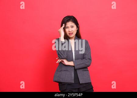 Asiatische Büromädchen, die ihre Arme vor Kopfschmerzen halten, während sie die Kamera mit einer grauen Jacke und einem roten Rock halten. Für die Gesundheit, Busin Stockfoto