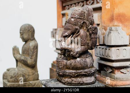 Eine Steinstatue von Ganesha, der hinduistischen elefantenköpfigen Gottheit, ist im Vordergrund zu sehen. Dahinter eine heitere Steinfigur eines Meditati Stockfoto