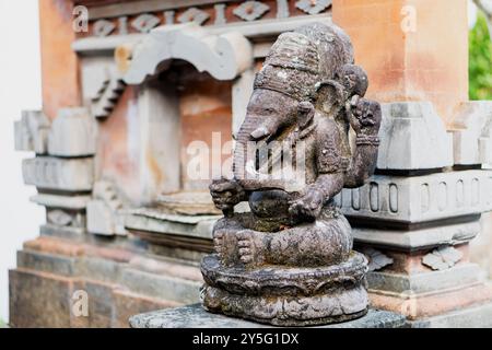 Eine Steinstatue von Ganesha, der Hinduelefantköpfigen Gottheit, sitzt auf einem Sockel. Die Statue ist aufwändig geschnitzt und verwittert und zeigt Details Stockfoto