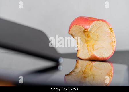 Eine Nahaufnahme eines gebissenen roten Apfels auf einer reflektierenden Oberfläche, mit einem verschwommenen Küchenutensil im Vordergrund. Der Apfel zeigt seine innere Konsistenz Stockfoto