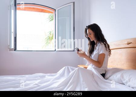 Frau, die morgens im Bett sitzt. Ausschalten der Weckerweiterung Stockfoto