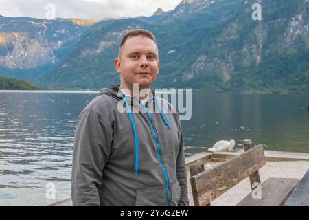 Ein 25-30-jähriger Mann steht an einem hölzernen Pier in der Nähe eines ruhigen Bergsees. Stockfoto
