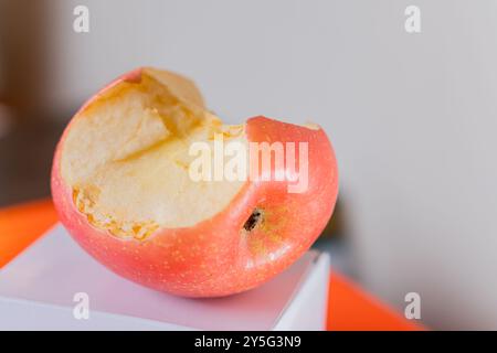 Ein teilweise gegessen roter Apfel, der auf einer weißen Oberfläche liegt und sein saftiges Inneres und seine lebendige Haut zeigt. Der Hintergrund ist leicht verschwommen und betont Stockfoto