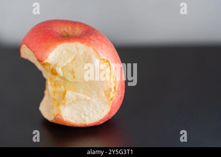 Ein teilweise gegessen roter Apfel, der auf einer schwarzen Oberfläche liegt. Der Apfel hat einen Biss, der sein helles Inneres offenbart. Der Hintergrund ist sanft bl Stockfoto