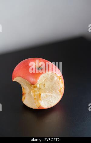 Ein gebissener roter Apfel auf einer schwarzen Oberfläche, der sein saftiges Inneres und seine lebendige Haut zeigt. Der Apfel ist glänzend und hat einen kleinen Biss Stockfoto